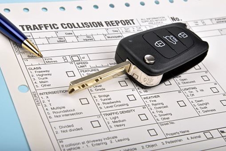 traffic collision report with car key and pen on top